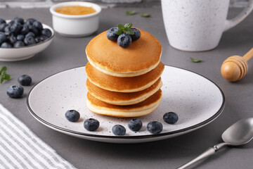 Delicious stack of pancakes topped with fresh blueberries and mint served with syrup on a gray tabletop