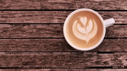 White ceramic coffee cup with tulip latte art on rustic wooden surface, creating a warm and cozy café atmosphere. Ideal for lifestyle, food, and social media content.