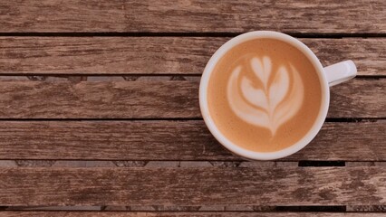 White ceramic coffee cup with tulip latte art on rustic wooden surface, creating a warm and cozy café atmosphere. Ideal for lifestyle, food, and social media content.
