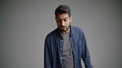 A confused man shrugs in a mid-shot video, wearing casual attire against a plain background, conveying uncertainty and questioning.