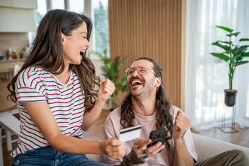 Happy couple celebrating online shopping success with credit card and smartphone