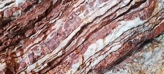 Close-up view of layered rock formations showing rich textures and natural striations in red, orange, and white tones, highlighting geological patterns and rugged surface details.
