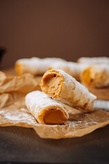 Caramel cream filled pastry rolls dusted with powdered sugar on parchment paper