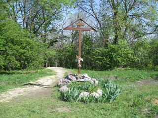 Wooden cross surrounded by stones and greenery in forest path  