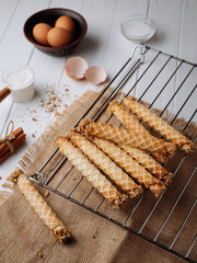Homemade wafer rolls with nuts on a cooling rack with baking ingredients, rustic setup