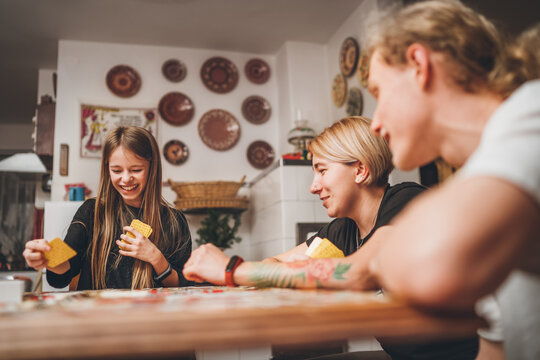 Cheerfully warm home togetherness cozy scene of family playing cards together in home kitchen. Girls and boys smiling and laughing with moms. Holidays time spending and relations concept image.