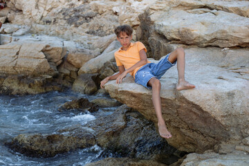 Boy sitting on seaside rocks. Boy sitting on seaside rocks by the water during summer vacation. 