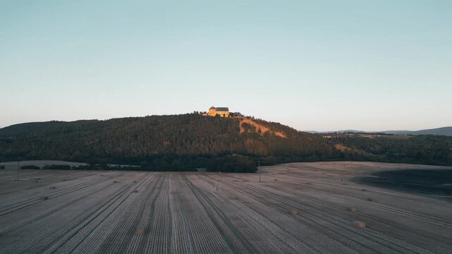 At dusk, Tocnik Castle stands majestically atop a hill, surrounded by golden fields. The summer sky casts a warm glow over this medieval ruin, creating a serene atmosphere.