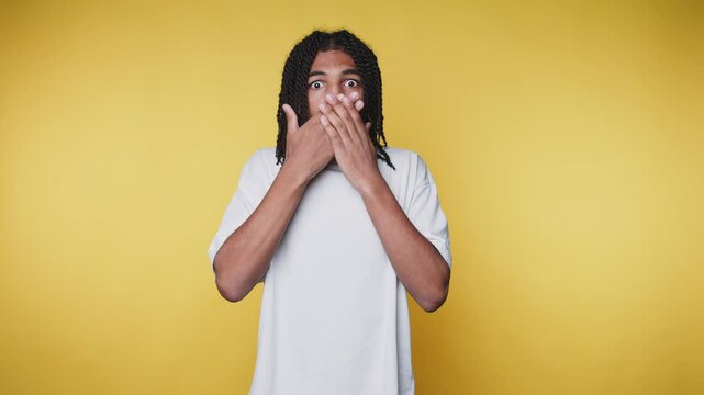 footage of young man reacts with surprise, covering his mouth on yellow background