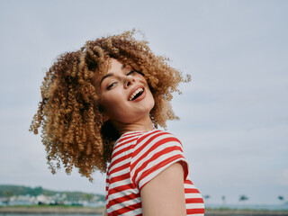 Joyful portrait of a woman with voluminous curly hair wearing a red and white striped shirt,...