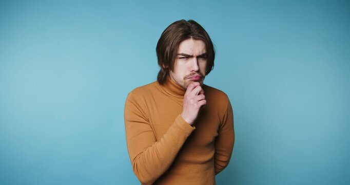 footage of young man in a turtleneck sweater gazes thoughtfully to the side, showcasing introspection and curiosity on blue background - Powered by Adobe