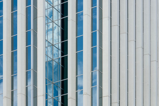 Detailed view of a modern high-rise building in downtown Saskatoon, Canada, showing vertical white lines and glass panels reflecting the sky and clouds.