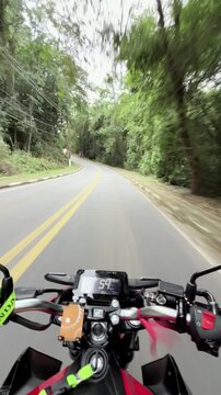 Passeio de moto em primeira pessoa por estrada sinuosa, com curvas e paisagem natural ao redor. Cena transmite liberdade, aventura e a emo&ccedil;&atilde;o de viajar na estrada.