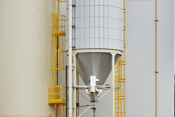 Close-up street level view of industrial storage silos with yellow metal ladders and pipes, photographed in Saskatoon, Canada.