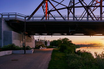 Golden sunset view of Saskatoon with a bridge crossing the river and high-rise buildings in the background.