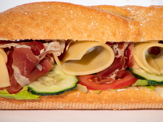 Fresh crispy baguette sandwich with ham, cheese, cucumber, tomato, salad.