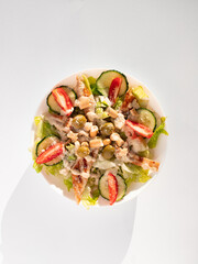 Caesar salad on a white plate with fresh vegetables, tomatoes, greenery, cucumbers, olives, cheese and sauce on a white background. View from above 