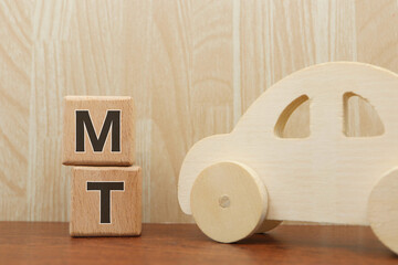 木製のおもちゃの車とMT表記ブロック。マニュアル車のイメージ。