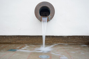 A steady stream of water flows from a circular metal spout into a shallow pool, creating a calm and...
