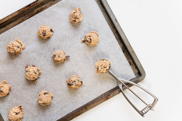 Round raw oatmeal raisin cookie dough scoops on sheet with baking paper made of flour, rolled oats, sugar, eggs, raisins and baking soda before baking with cookie dough scoop on white background