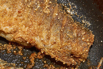 Roast crucian carp. A close-up of an appetizing piece of fish fried until golden crisp in breadcrumbs in a frying pan. A traditional homemade dish made with aromatic spices and oil.