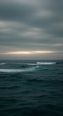 Obraz premium A moody seascape with dark, rolling waves under a brooding, overcast sky. A hint of pale light appears on the horizon. The overall atmosphere is serene yet somewhat melancholic.