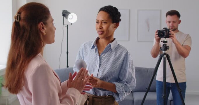 Studio interview and discussion of talking journalist holding microphone and female guest. Friendly dialogue of professional reporter and woman, operator filming video interview with camera on tripod
