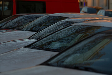 A closeup view captures a row of parked cars featuring fogged windows, beautifully showcasing a typical city street scene bathed in the soft, golden light of the early morning hours