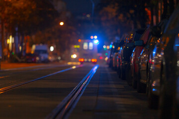 At midnight on a calm street, parked cars align perfectly as police lights flicker on the pavement, showcasing urban life and the vital role of emergency services in community safety