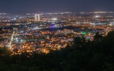 Fototapeta premium night cityscape from a high vantage point, with the glowing lights of a bustling city stretching to the horizon. A prominent skyscraper stands out 