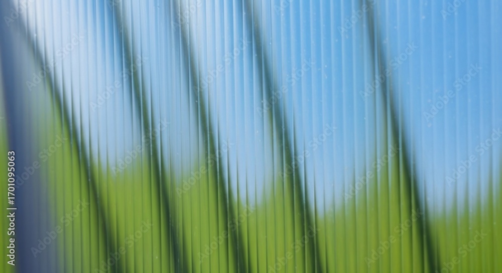Poster abstract background of a translucent corrugated panel with a blurred view of a green field and blue 