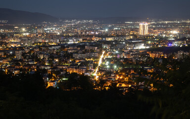 panoramic night view of a sprawling european city from a hill, with city lights, illuminated buildings, and a glowing main street. taken in skopje, macedonia