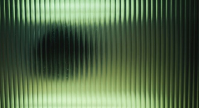 Abstract background of a mysterious dark silhouette seen through a green fluted or ribbed glass panel. Modern textured backdrop with vertical lines and light.