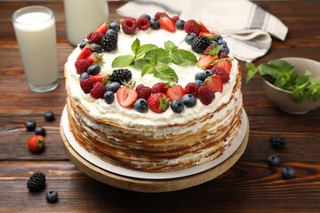 Delicious crepe cake with fresh berries and milk on wooden table, closeup