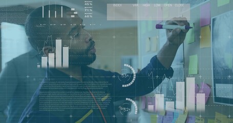 Man in blue sweater marking sticky notes with purple marker on partition in office, data analysis