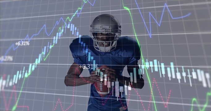 American football player in silver helmet and blue jersey holding football in studio, with charts