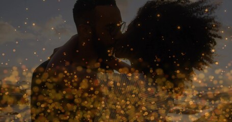 Embracing couple wearing striped top, dark shirt with eyeglasses on beach at sunset, bokeh effect