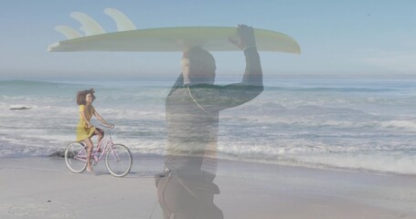 Wetsuit-clad man carrying surfboard, yellow-dress woman pedaling bicycle on beach, ocean waves