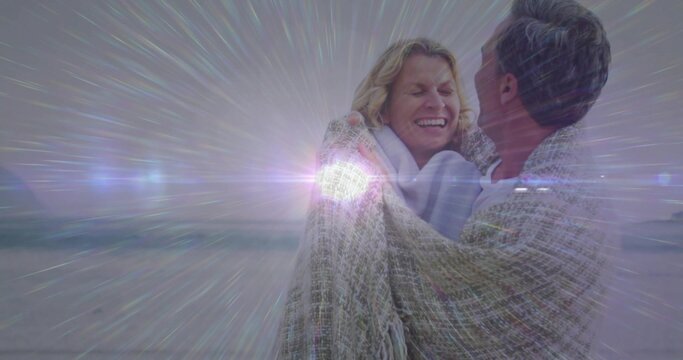 Embracing middle-aged couple holding each other on sandy beach at dusk, with woven blanket
