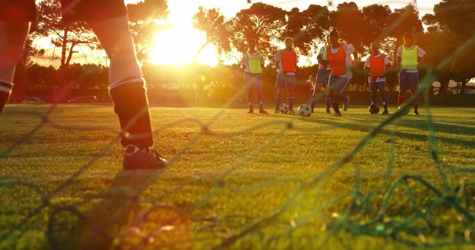 Standing goalkeeper wearing neon bib on field at sunset, with goal net, soccer balls, copy space