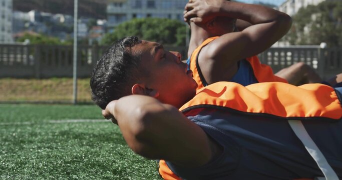 Performing sit-up exercises soccer players lying on turf field, with training bibs, athletic shorts - Powered by Adobe
