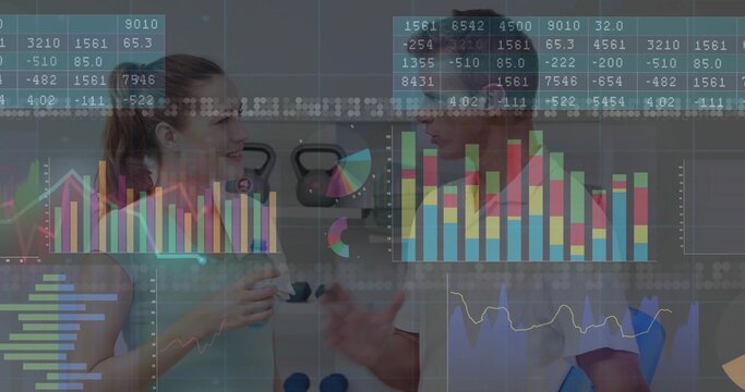 Standing trainer and client analyzing digital charts in gym, showing water bottle and kettlebells