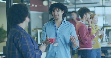 Gesturing man in light blue shirt ID badge holding red mug talking in break area