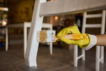 Engage in DIY chair restoration using a paint brush and protective gloves for the process