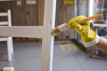 Engage in DIY chair restoration using a paint brush and protective gloves for the process