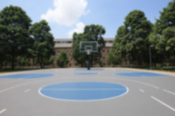 Blurry image of a modern basketball court located in the courtyard of a university building and there are many trees planted around it, blurred background.