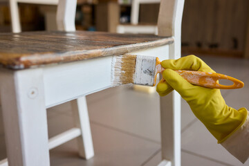 Engage in DIY chair restoration using a paint brush and protective gloves for the process