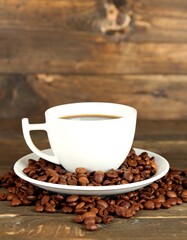 Coffee cup filled with dark liquid, surrounded by coffee beans on a wooden table