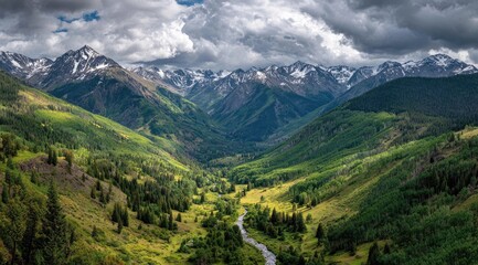 Naklejka premium Mountain valley with snow-capped peaks, vibrant green slopes, and a winding river. Vast expanse of a rugged, alpine landscape under a dramatic sky