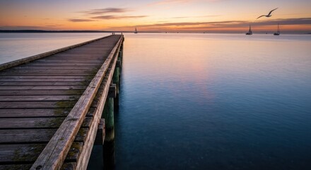 Sunrise pier extending over calm water, sailboats visible in distance